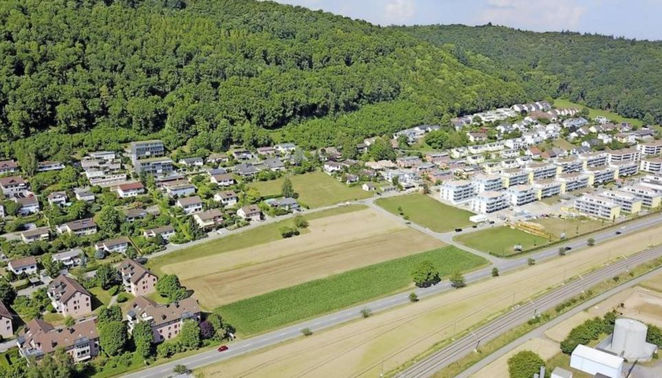 Links neben den Neubauten Underem Benze, auf dem länglichen grün-braunen Feld, wird der neue Benzepark entstehen. Auf ihm werden ein Spielplatz, eine Hütte mit Grillstelle sowie eine Pumptrack-Anlage für Velofahrer erstellt. Bild: Michael Kessler