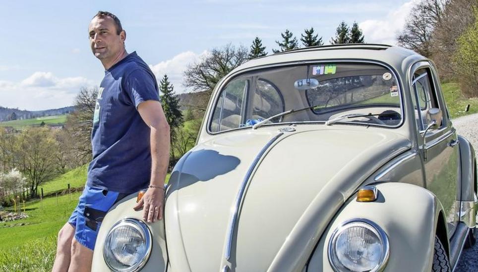 Ein Mann und sein Käfer: Raphael Niedermann steht mit seinem VW auf dem Feld gegenüber von der Büsinger Kirche. Bild: Begüm Ürek