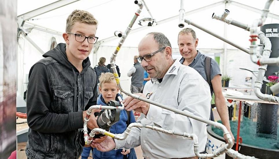 Walter Heller und Silas beobachten, wie Tobias mithilfe von Hans Jakob Bickel die Röhrenskulptur erweitert.