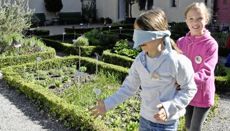 Die Zweitklässlerinnen Emma und Lilli führen sich abwechselnd mit verbundenen Augen durch den Kräutergarten des Münsters. Bild: Melina Ehrat