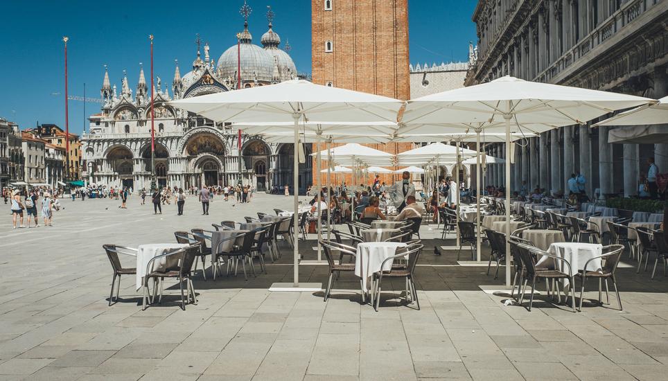 Piazza San Marco: das kaum besetzte Cafe Florian mit Kellnern in Frack und blauer Maske. Im Hintergrund der Markusdom. Bild: Roberta Fele