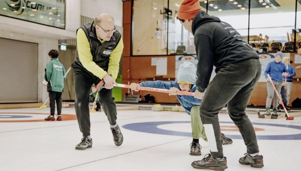 Peter Lengweiler und Aagne Chaturvedi üben die richtige Haltung bei der Abgabe, indem sie ein Kind an einem Curlingbesen übers Eis ziehen. Bilder: Roberta Fele