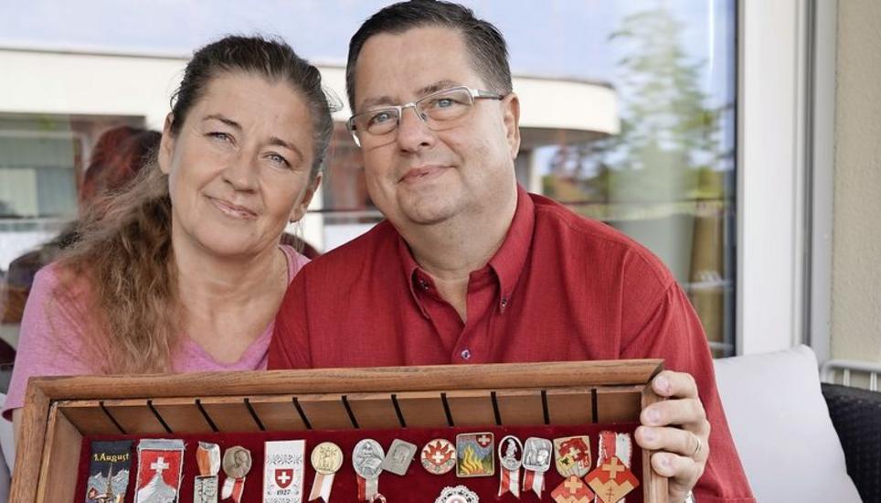 Alfred Marty posiert mit seiner aus Litauen stammenden Frau und den vollzähligen 1.-August-Abzeichen. Das allererste ist sein Favorit. Bild: Tobias Bolli