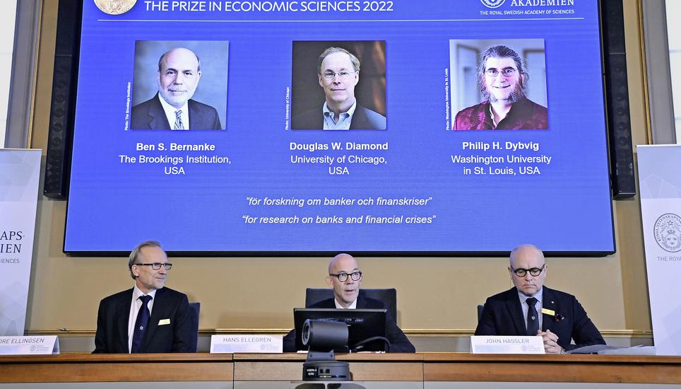 Die Porträtbilder von Ben Bernanke, Douglas Diamond und Philip Dybvig (v. l.) erscheinen auf blauem Hintergrund in der Präsentation zur diesjährigen Vergabe des Wirtschaftsnobelpreises. Darunter sprechen die Vertreter der Königlich Schwedische Akademie der Wissenschaften zu den Medien. Bild: Key