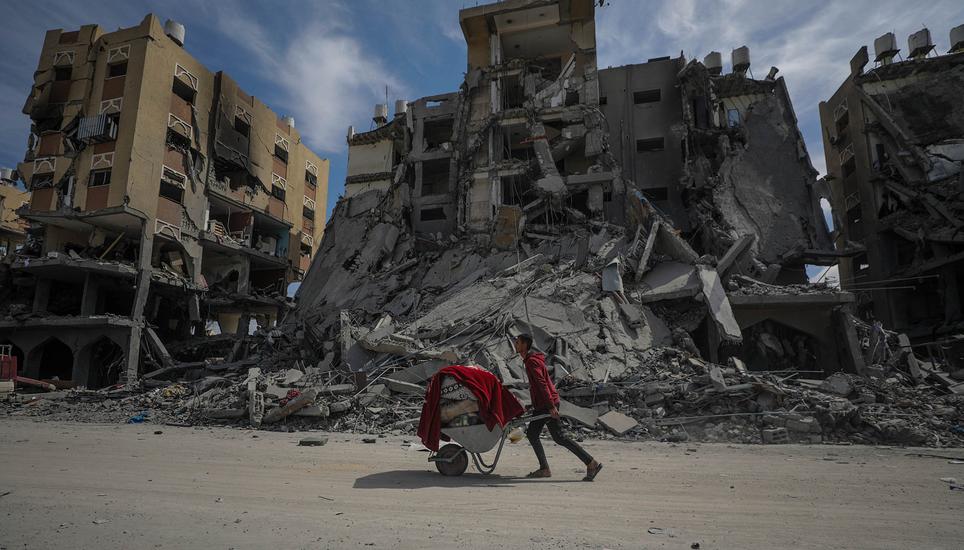 epaselect epa11220424 A Palestinian man pushes a wheelbarrow past the rubble of destroyed houses at Hamad towers city following an Israeli military operation in Khan Younis town, southern Gaza Strip, 14 March 2024. More than 31,000 Palestinians and over 1