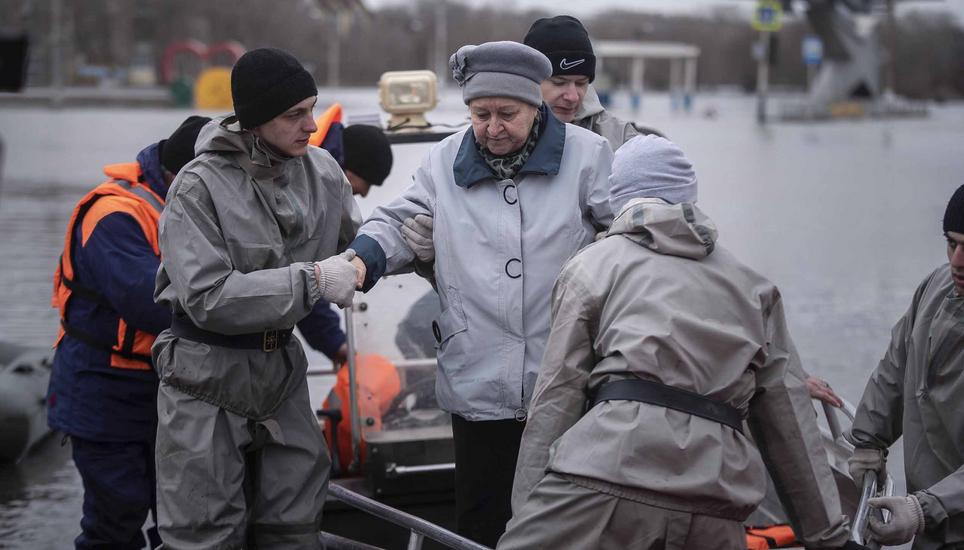 Emergency workers assist a woman to deboard a boat during evacuations local residents in a flooded street after a part of a dam burst, in Orsk, Russia on Monday, April 8, 2024. Floods caused by rising water levels in the Ural River broke a dam in a city n