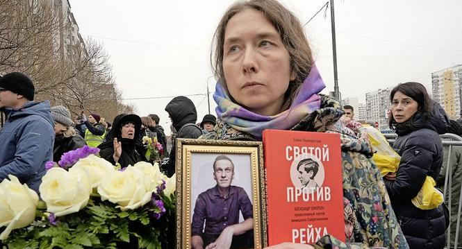 A woman holds a portrait of Alexei Navalny and a book titled "A saint against the Reich" as people gather outside the Church of the Icon of the Mother of God Soothe My Sorrows, in Moscow, Russia, Friday, March 1, 2024. Relatives and supporters of Alexei N