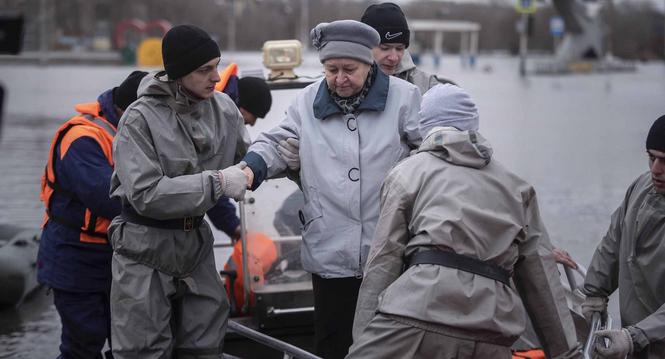 Emergency workers assist a woman to deboard a boat during evacuations local residents in a flooded street after a part of a dam burst, in Orsk, Russia on Monday, April 8, 2024. Floods caused by rising water levels in the Ural River broke a dam in a city n
